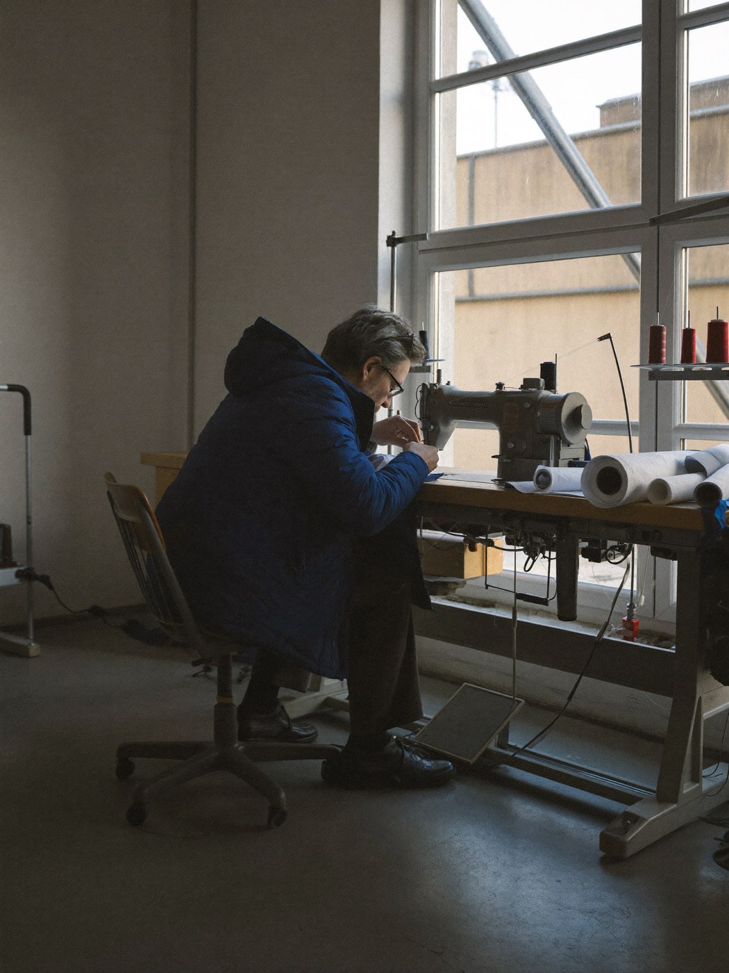 Craftsman stitching a navy parka shell at an industrial sewing machine in the bergen workshop